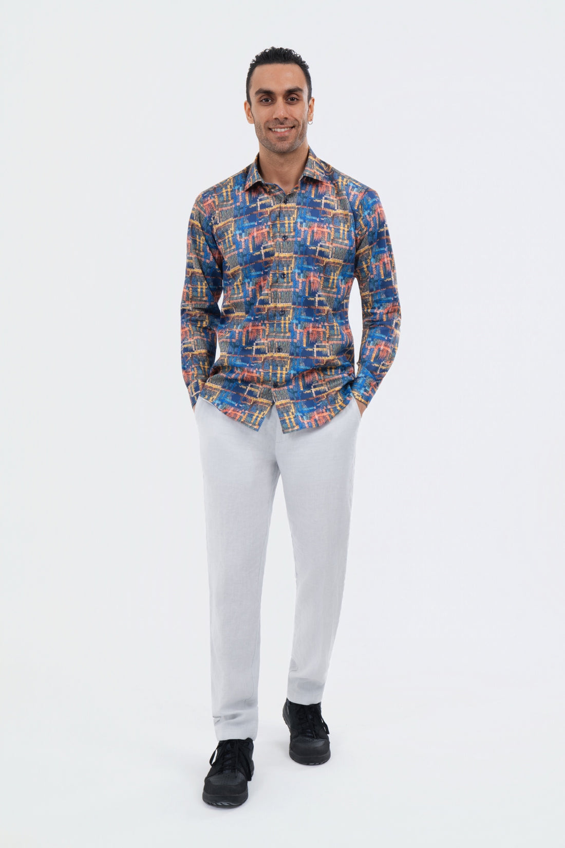 Male model wearing an orange and blue abstract-print shirt with white trousers.