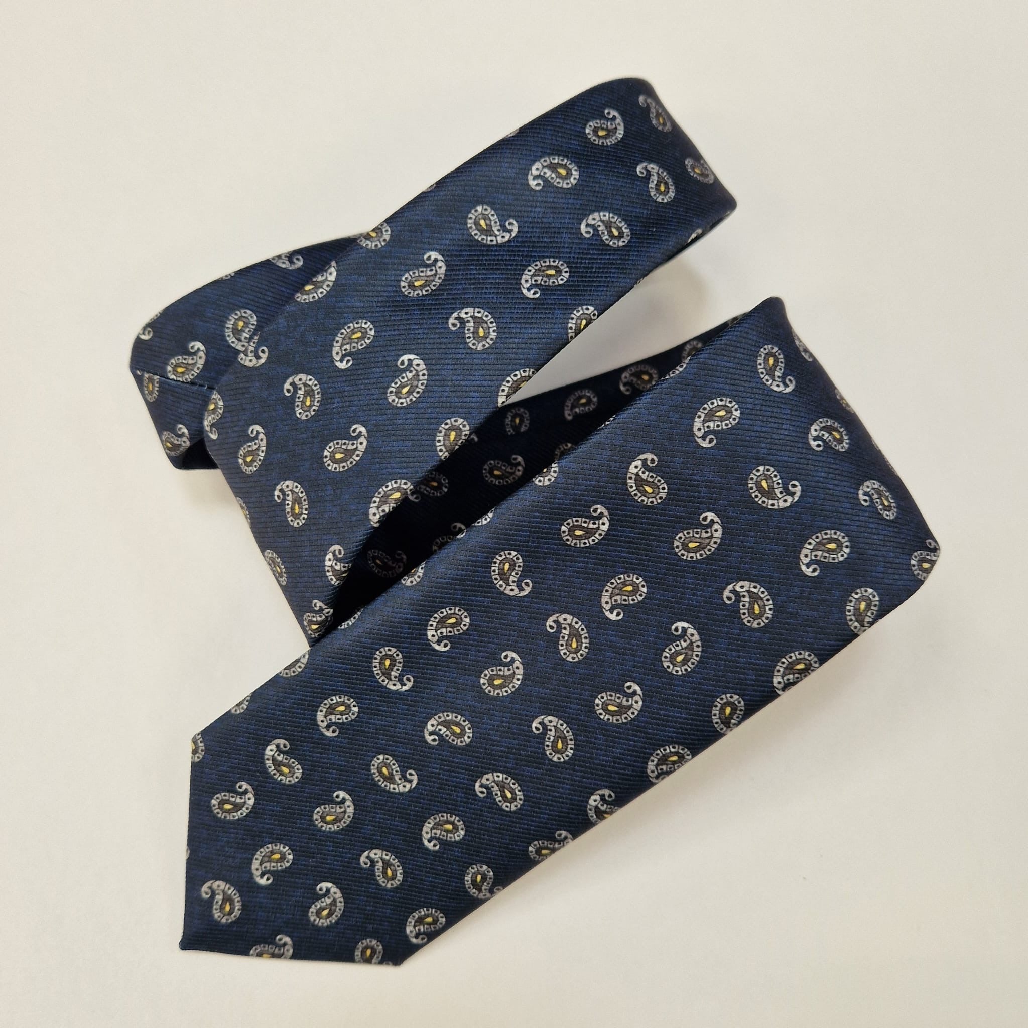 Navy silk tie with small silver paisley motifs, loosely folded.