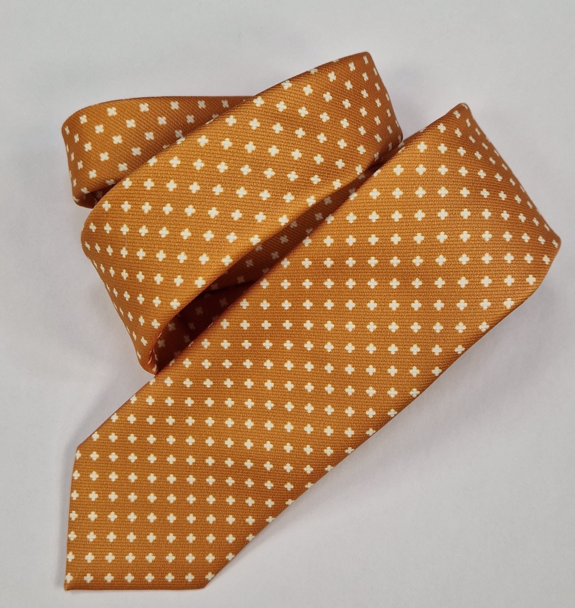 Ochre silk tie with a small white cross pattern, loosely folded.